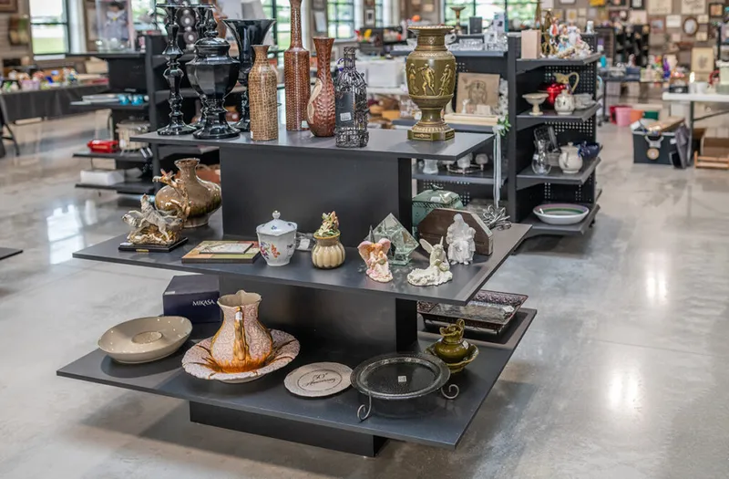 Tiered black display shelves holding vases, porcelain figurines, and decorative dishes inside a thrift store