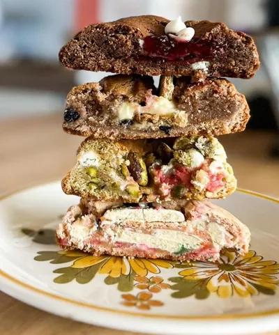 Stack of halved stuffed cookies with colorful fillings on a floral plate