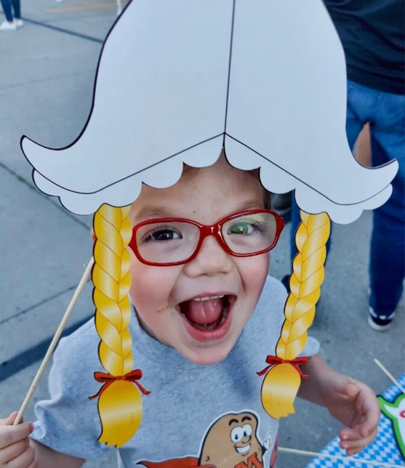 Laughing young child holding a cardboard Oktoberfest dirndl photo prop with braids