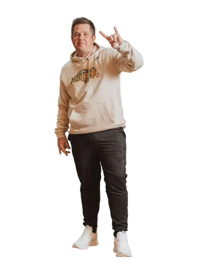 Man in a cream graphic hoodie and dark joggers making a hand gesture