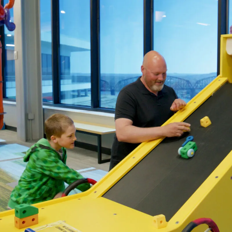 Adult and young boy playing together at a yellow ramp exhibit inside a children's museum