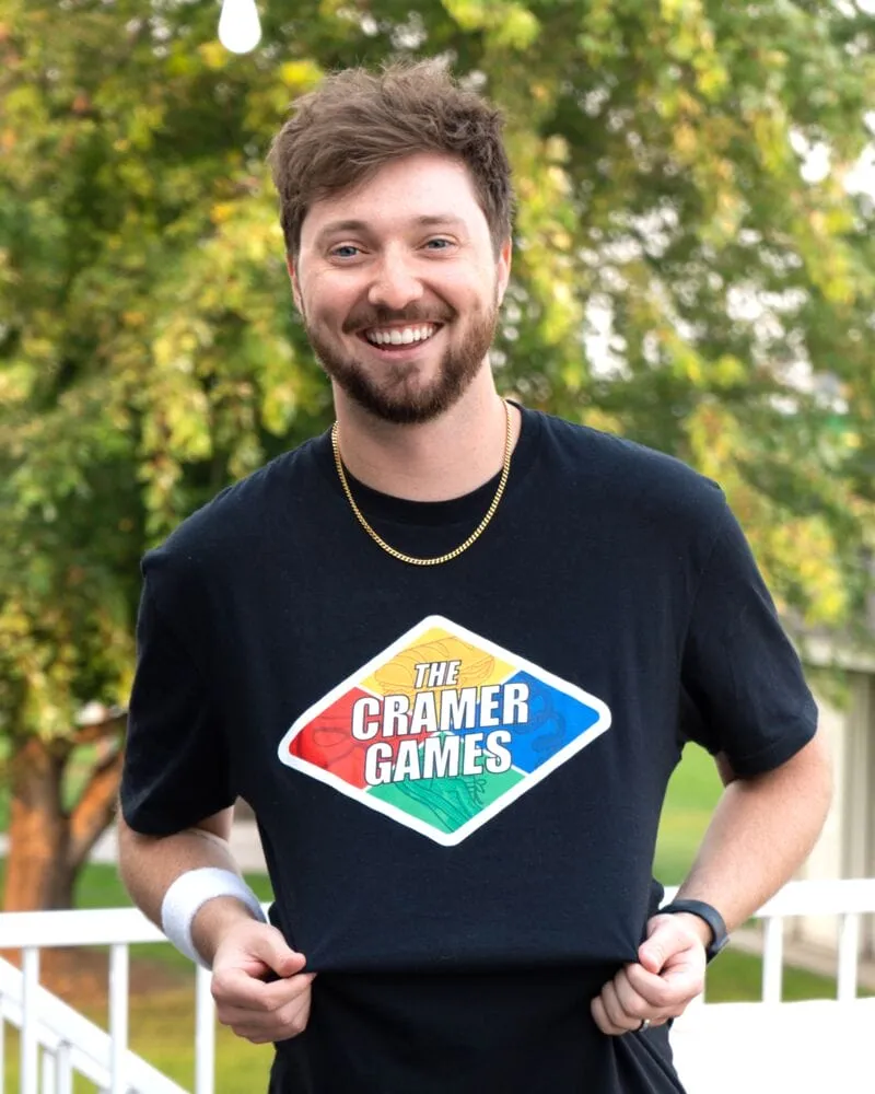 Smiling bearded man in a black 'The Cramer Games' T-shirt outdoors