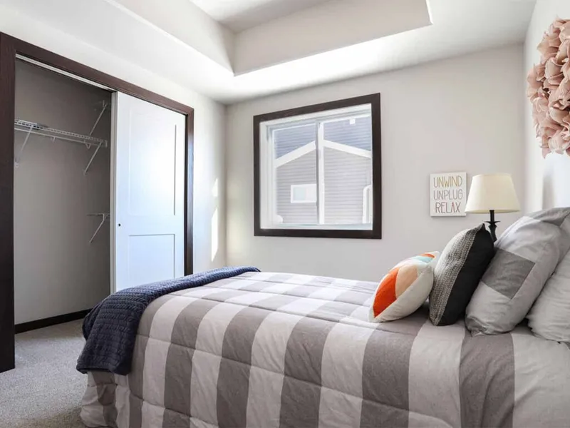 Bedroom with gray striped bedding, open closet, and framed window