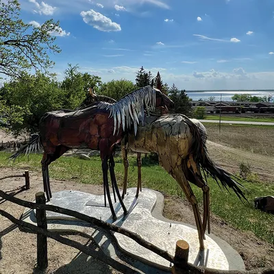 Two metal horse sculptures on a platform overlooking a lake on a sunny day
