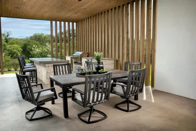 Covered patio with dark metal dining set and outdoor kitchen amid wood slat walls