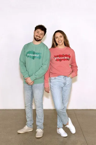 Man in green graphic sweatshirt and woman in pink graphic sweatshirt posing together