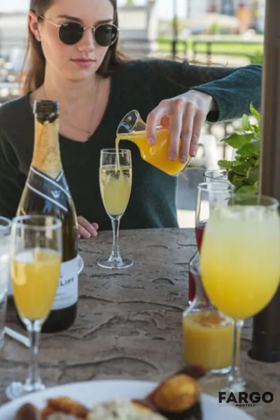 Woman in sunglasses pouring orange juice into a champagne flute at an outdoor patio table
