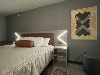 Hotel guest room with leather headboard, V-shaped accent lights, and geometric wood wall art