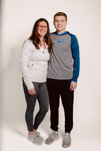 Woman in white zip-up jacket and teen boy in gray hoodie posing together against white background