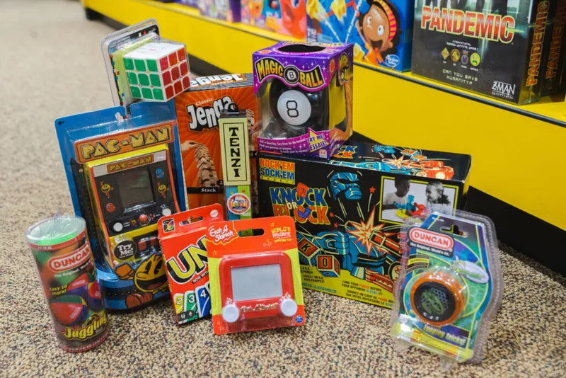 Assortment of classic toys including Pac-Man arcade, Magic 8 Ball, Etch A Sketch, Uno, Rubik's Cube, and yo-yo