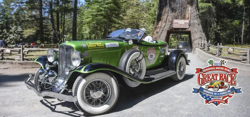 Green vintage roadster passing through a drive-through redwood tree tunnel