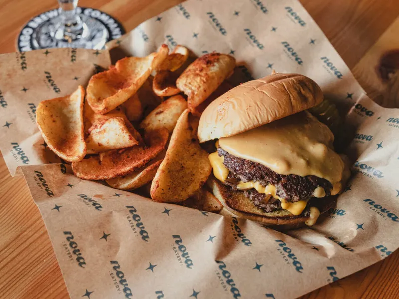 Cheeseburger with melted cheese and potato wedges on branded deli paper