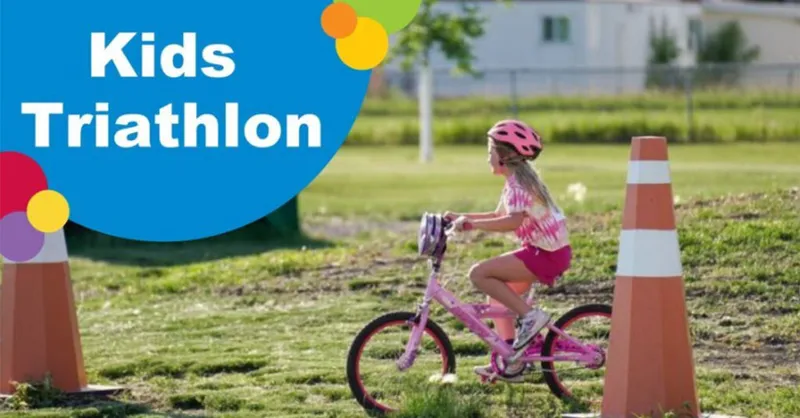 Young girl in pink helmet rides a pink bike between orange traffic cones at a kids triathlon event