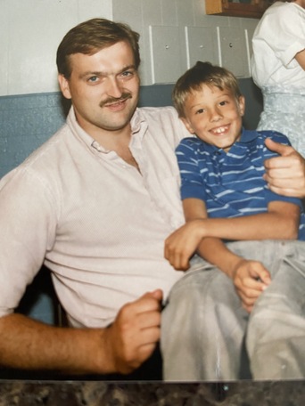 Mustachioed man in pink shirt sitting beside a smiling young boy giving a thumbs up