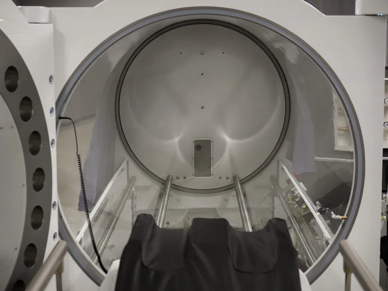 Interior view of an open hyperbaric oxygen chamber with metal rails and a rounded white hull