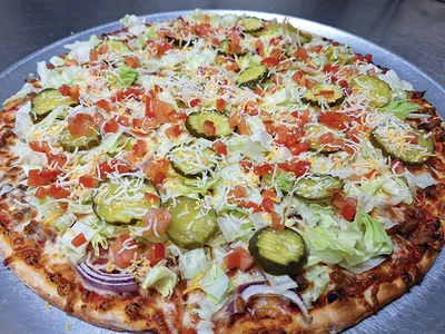 Pizza topped with shredded lettuce, pickle slices, diced tomatoes, onions, and cheese