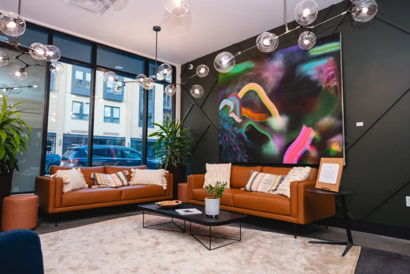 Two tan leather sofas face a bold colorful abstract painting on a dark geometric accent wall in a modern lobby