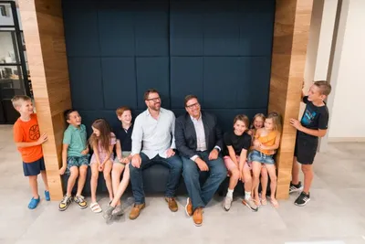 Two men seated on a bench surrounded by eight smiling children in a modern interior