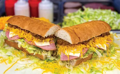 Two halves of a sub sandwich loaded with ham, shredded cheese, and lettuce on a hoagie roll
