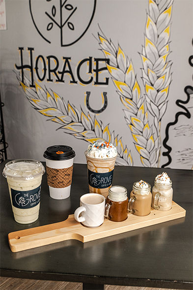 Assorted coffee drinks on a wooden board in front of a painted 'Horace' mural