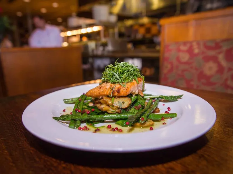 Seared salmon fillet over green beans and mushrooms topped with fresh herbs on a white plate