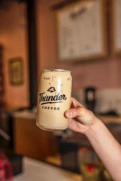 Hand holding a can-shaped glass of iced latte branded Thunder Coffee