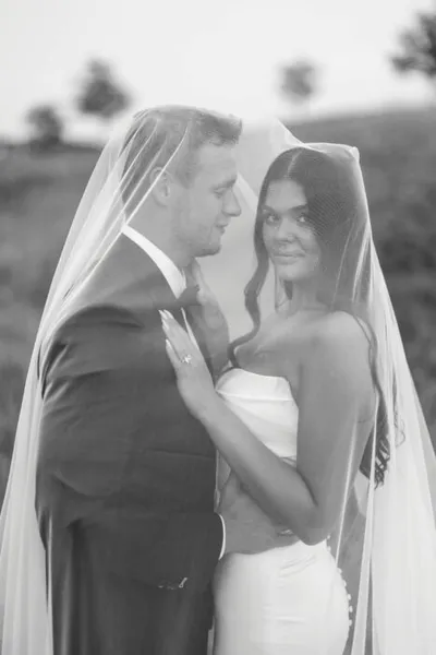 Bride and groom sharing an intimate moment under a flowing veil, black and white