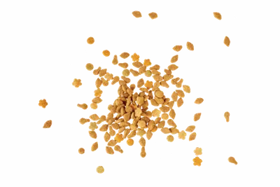 Small pile of golden fenugreek seeds scattered on a white background