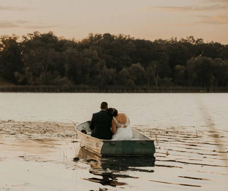 Bride and groom sitting together in a small rowboat on a calm lake at sunset