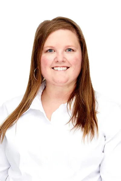 Smiling woman with long auburn hair wearing a white button-up shirt against a white background