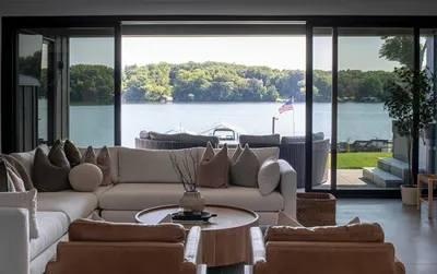Modern living room with cream sectional sofa and floor-to-ceiling glass doors opening to a lakeside view