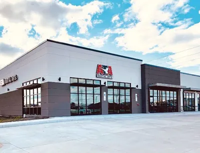 Modern retail storefront with large windows and a red logo sign under a cloudy sky