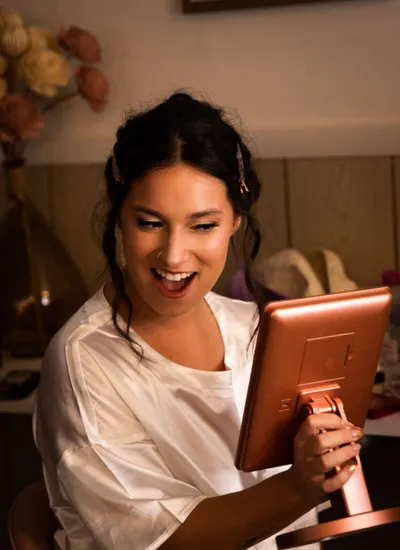 Smiling woman in white satin robe holding a rose-gold handheld mirror