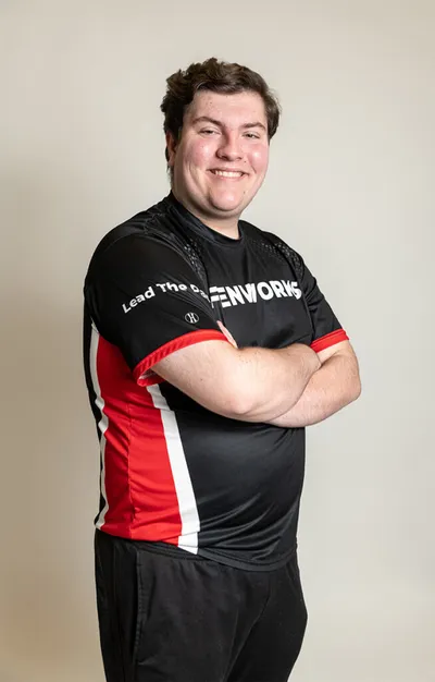 Smiling young man in a black, red, and white Fenworks esports jersey, arms crossed