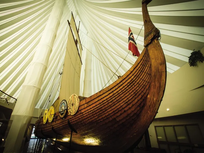 Wooden Viking longship with white sail and Norwegian flag displayed inside a museum