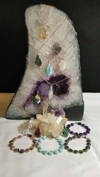Gemstone pendants displayed on an amethyst geode with crystal and beaded bracelets arranged in front