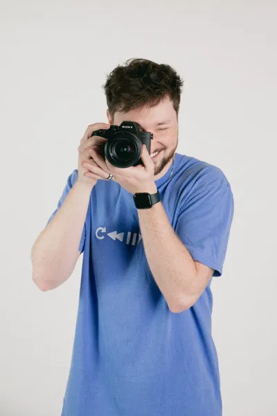 Smiling young man in blue T-shirt holding a Sony camera up to his eye
