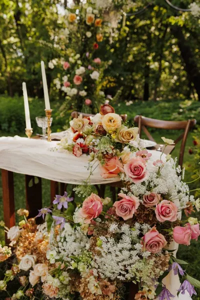Outdoor wedding table draped in white linen, adorned with pink roses and candles amid lush greenery
