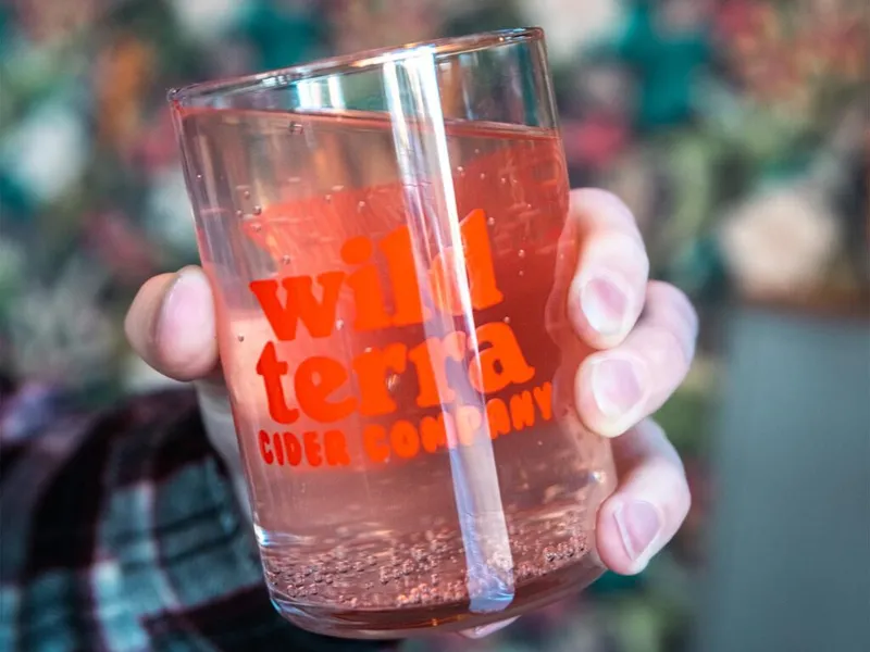 Hand holding a glass of pink sparkling cider branded Wild Terra Cider Company