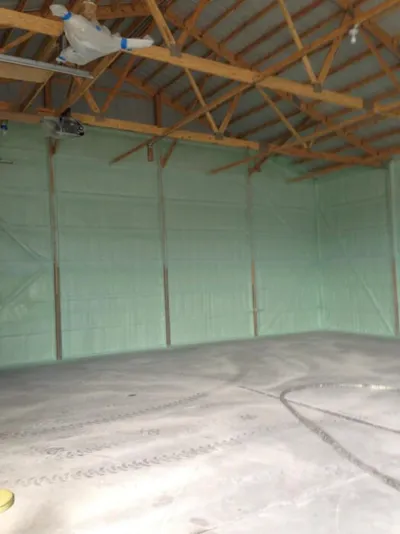 Empty building interior with green spray foam insulation on walls and exposed wooden roof trusses