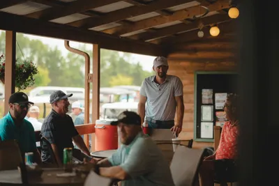 Group of people gathered under a rustic covered porch at a lakeside resort