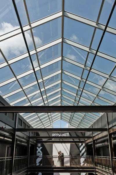 Couple standing on an indoor balcony beneath a soaring glass-panel skylight roof