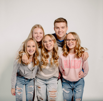 Five smiling teenagers pose together in casual sweatshirts and jeans against a white background