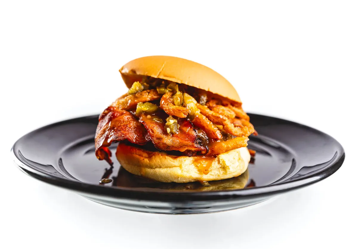 BBQ sandwich with bacon and diced jalapeños on a black plate
