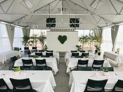 Banquet hall with white-draped tables, black chairs, and a moss heart display at the front