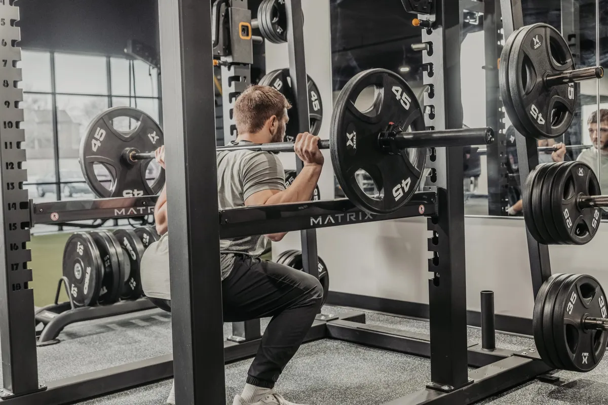 Man performing barbell squats in a squat rack at a modern gym