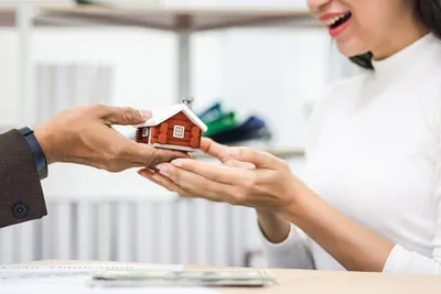 Two people exchanging a small red model house across a desk