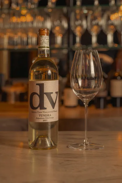 Bottle of DV Tundra white wine beside an empty wine glass on a bar counter