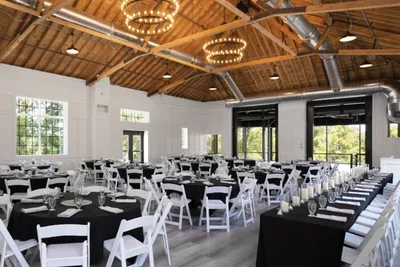 Bright event hall with wood-beam ceiling, chandelier rings, round black-draped tables, and white folding chairs