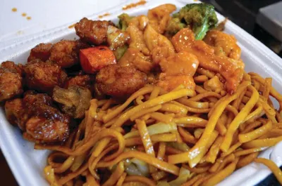Takeout container filled with lo mein noodles, sauced shrimp, and fried chicken with vegetables
